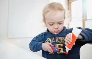 Criança segurando escova de dentes e creme dental